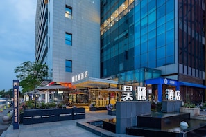 Un hotel moderno con fachada de vidrio, zona de estar al aire libre y señalización en un idioma extranjero.