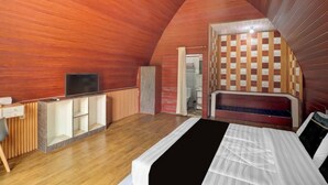 Quarto com teto inclinado, uma cama, televisão, escrivaninha e guarda-roupa.