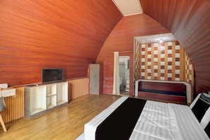 Ein Schlafzimmer mit schrägverdeckter Decke, einem Bett, einem Fernseher, einem Schreibtisch und einem Kleiderschrank.