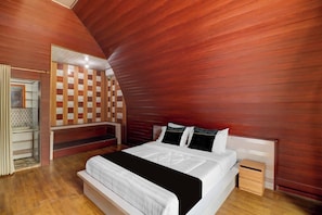 A bedroom with a sloped ceiling, a bed with white bedding, a wooden headboard, and a small bedside table.