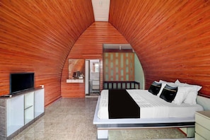 Ein Schlafzimmer mit schrägem Dach, einem Bett mit weißer Bettwäsche, einem Fernseher auf einem Schrank und einem Badezimmer mit Spiegel und Waschbecken.