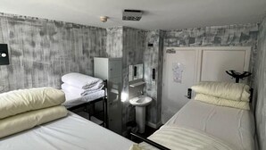 Hotellihuone, jossa on kaksi sänkyä, pieni pesuallas ja vaatekaappi.