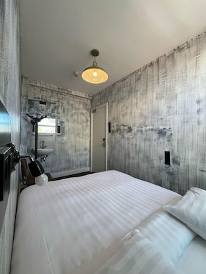 A hotel room with a bed, a bedside lamp, a wall-mounted sink, and a door. - Amigo Budget Hotel (Amsterdam)