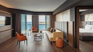 Une chambre d’hôtel moderne avec un grand lit, un canapé, deux fauteuils, une petite table ronde et une vue sur la mer.