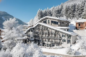 Ein modernes Skiresort-Gebäude mit mehreren Balkonen und großen Fenstern, umgeben von schneebedeckten Bäumen und Bergen.