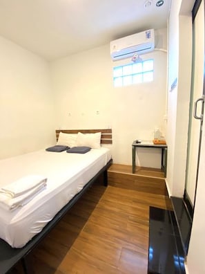 A small, single-bed room with a wooden floor, a bedside table, and a window with blinds. - TAB Hotel Malioboro Yogyakarta (Yogyakarta)