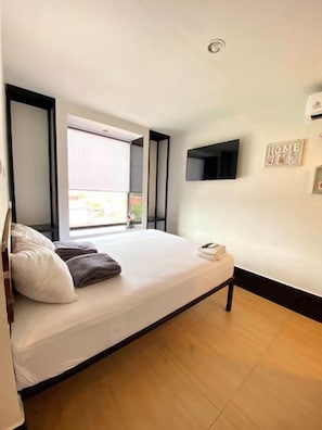 Ein Schlafzimmer mit Bett, Fenster, einem an der Wand befestigten Fernseher und einer Wandklimaanlage.