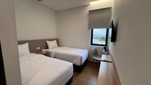 A hotel room with two beds, a desk, a chair, a TV, and a window with a view. - Yes Hotel (Bandar Lampung)