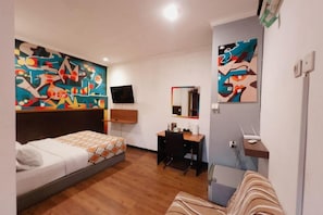 Habitación de hotel con cama, escritorio, silla, televisor y obras de arte en las paredes.