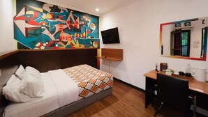 Une chambre d’hôtel équipée d’un lit, d’un bureau, d’une chaise, d’un miroir et d’un téléviseur fixé au mur.