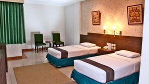 Ein Hotelzimmer mit zwei Betten, einem Schreibtisch, zwei Stühlen, einem kleinen Tisch und einem Nachttisch mit Lampe.