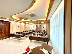 Un salón de conferencias con mesas y sillas, una puerta de madera y un ventanal con cortinas.