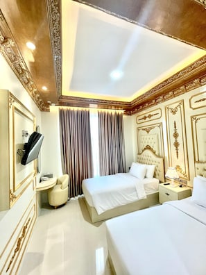 Una habitación de hotel con una cama grande, una cama más pequeña, un tocador con espejo, un televisor y un escritorio con lámpara.