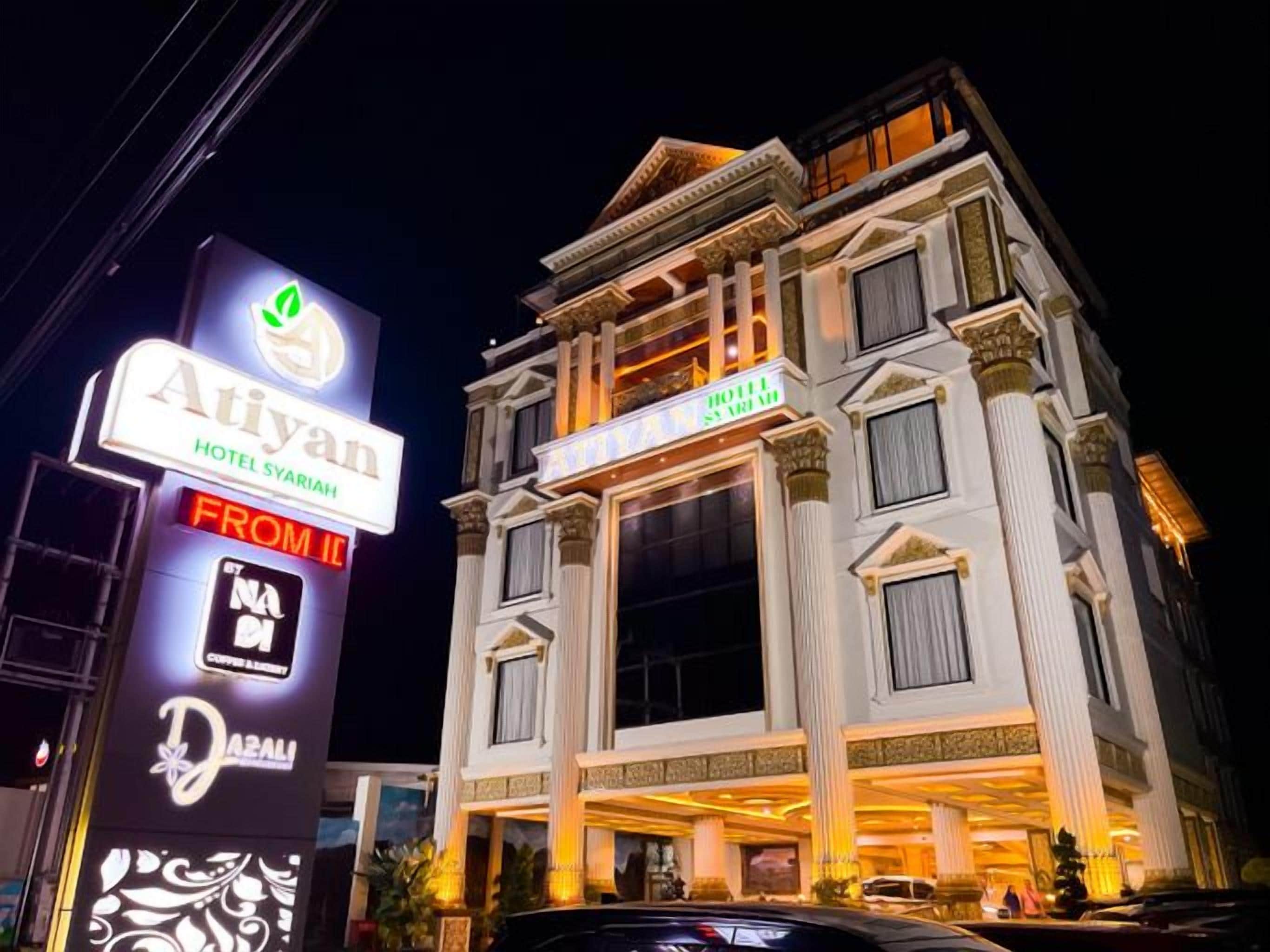 A multi-story hotel with a classical architectural style, featuring a prominent entrance and illuminated signage.