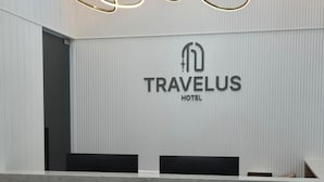 Ein moderner Empfangstresen mit dem Schriftzug TRAVELUS HOTEL darüber.