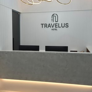 Un taulell de recepció de disseny modern, amb el logotip de TRAVELUS HOTEL a la part superior.