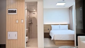 Ein modernes Hotelzimmer mit einem Glastisch, einem Bett mit weißer Bettwäsche, einem Holz-Kopfteil und einem Badezimmer mit Dusche und Toilette.