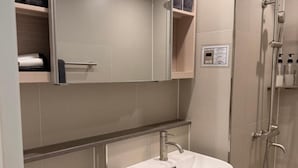Ein Badezimmer mit einem weißen Waschbecken, einem Spiegel, einem Handtuchhalter und einer Duschkabine.