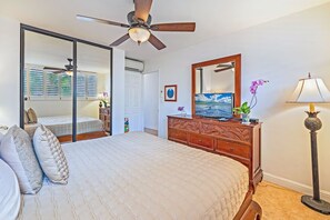 A bedroom with a bed, a dresser, a mirror, a ceiling fan, and a window with blinds. - Turtles, Whales & Waves from Oceanfront Private Lanai (Wailuku)