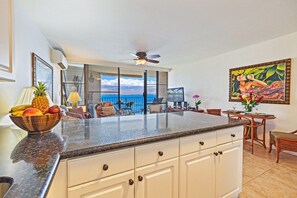 A kitchen with a large island, white cabinetry, and a view of the ocean. - Turtles, Whales & Waves from Oceanfront Private Lanai (Wailuku)