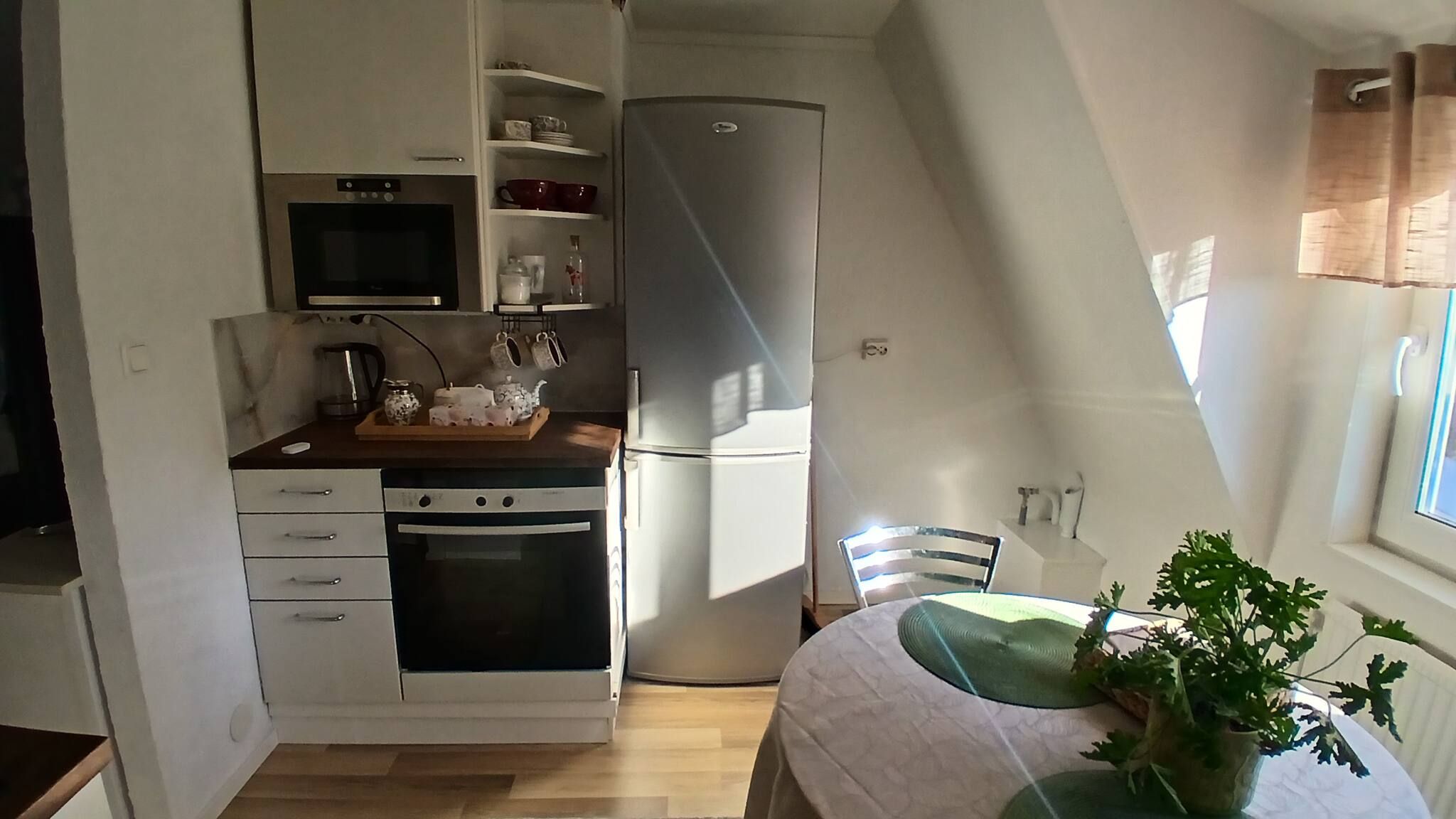 Eine kompakte Küche mit Mikrowelle, Backofen und Kühlschrank. Ein Essbereich mit Tisch und Stühlen lädt zum Verweilen ein, und ein Blumentopf steht auf der Fensterbank.