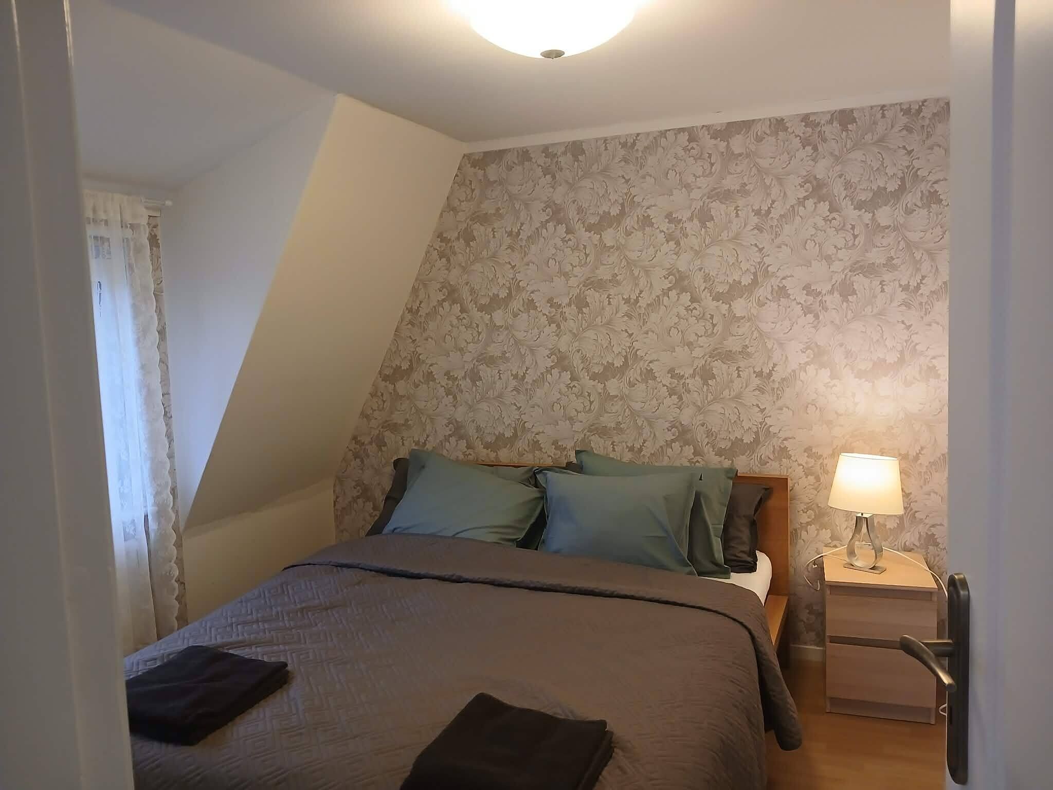 A bedroom with a bed, pillows, a nightstand, and a lamp.