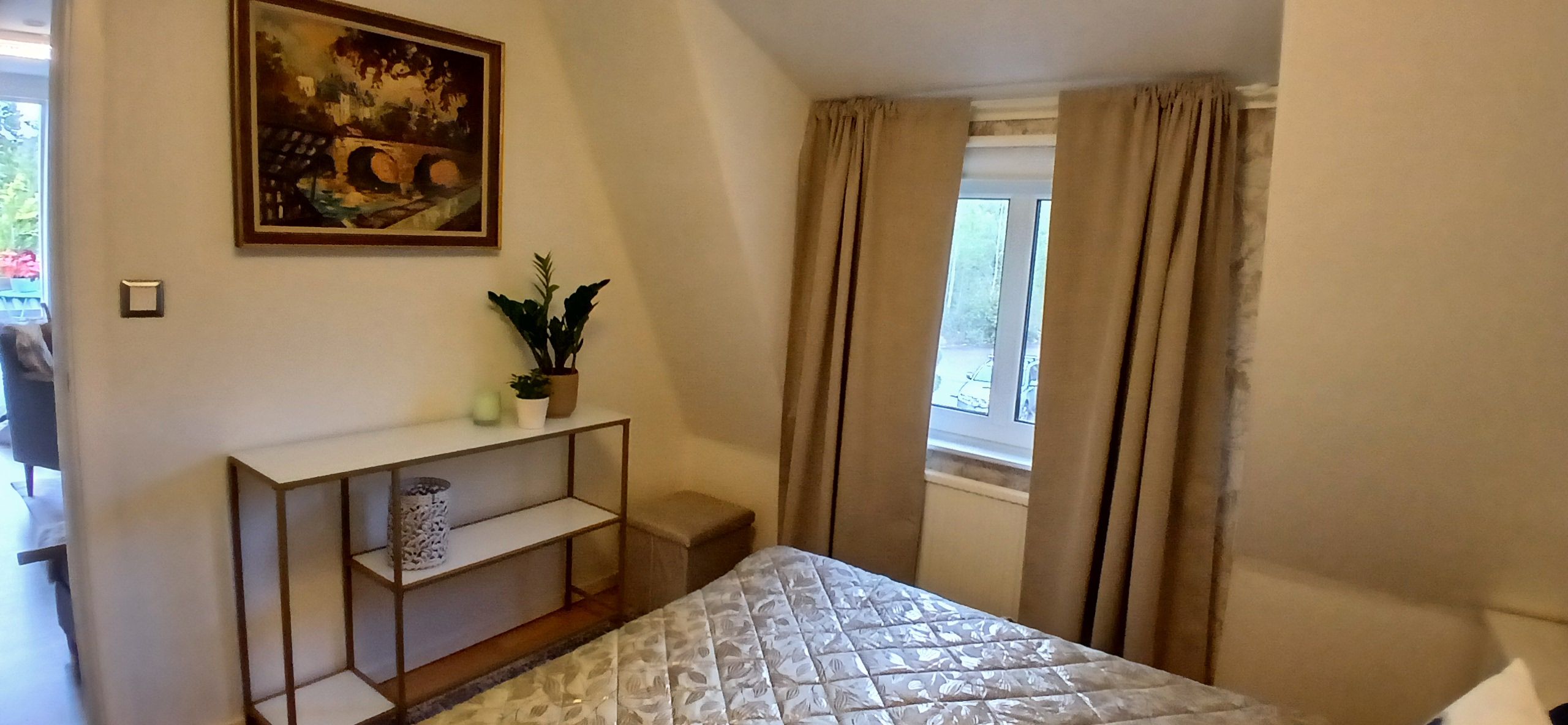 Ein Schlafzimmer mit einem Bett, einem Nachttisch mit Pflanze, einem Bild an der Wand und einem Fenster mit Vorhängen.