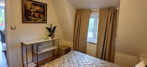 Ein Schlafzimmer mit einem Bett, einem Nachttisch mit Pflanze, einem Bild an der Wand und einem Fenster mit Vorhängen.