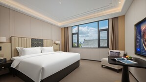 Ein Hotelzimmer mit einem großen Bett, einem Schreibtisch mit Stuhl, einem Fernseher und einem Fenster mit Blick auf die Stadt.