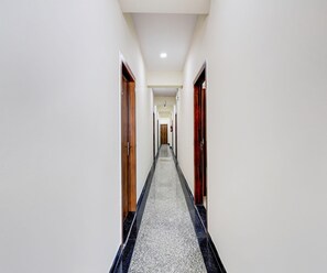 A long, narrow hallway with white walls and a grey carpet. - Deluxe Room Collection O Sadar Bazaar (Gurugram)