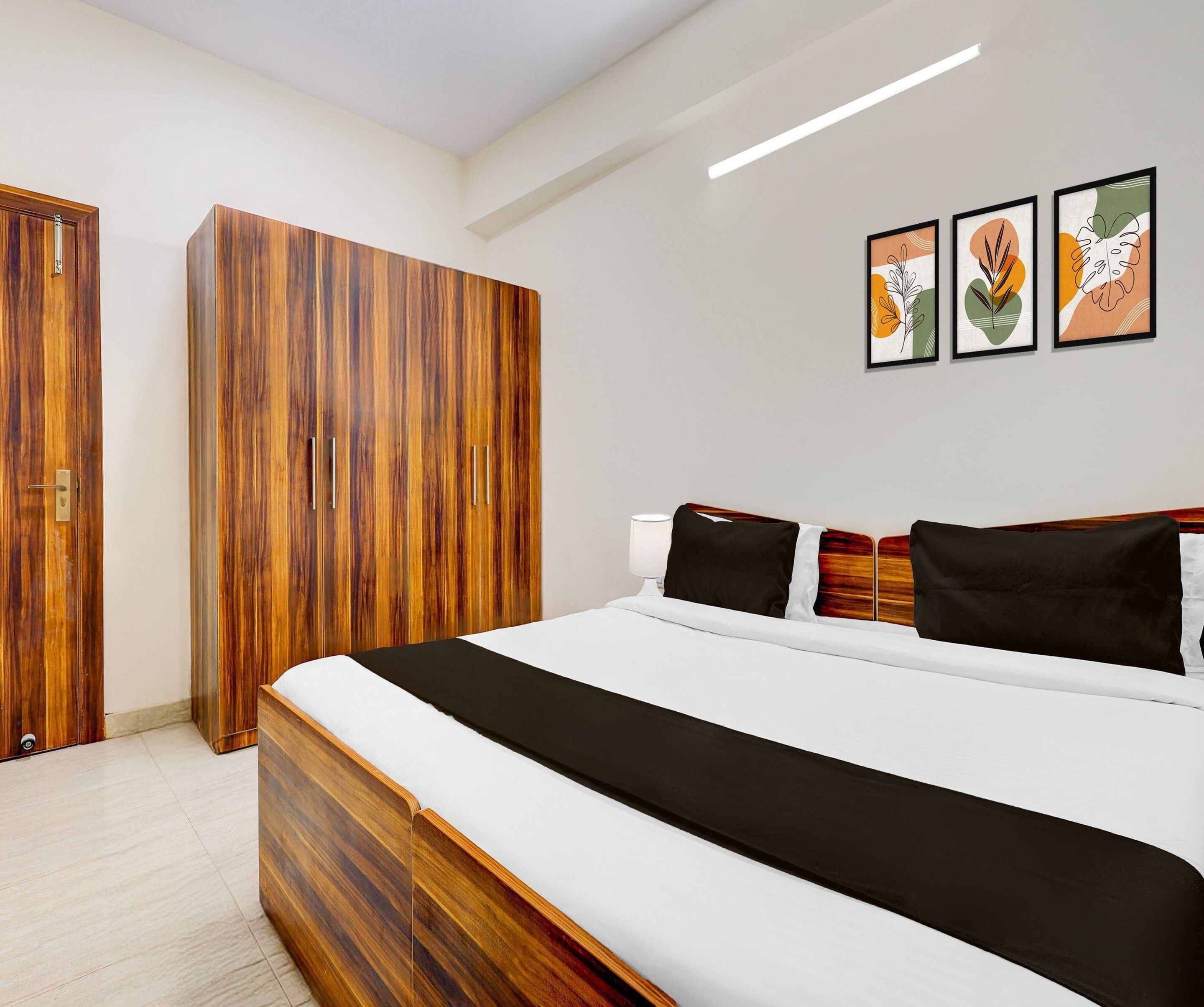 A modern bedroom with a wooden wardrobe, a bed with white bedding, and three framed artworks on the wall.