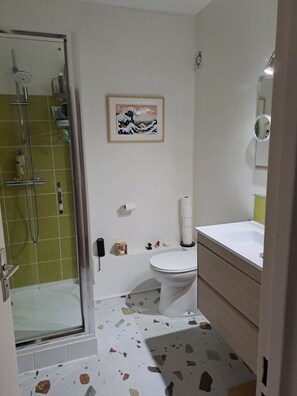 Ein Badezimmer mit Duschkabine aus Glas, Toilette, Waschbecken und einem gerahmten Kunstwerk an der Wand.
