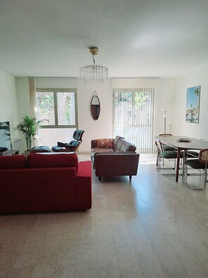 Een ruime woonkamer met een rode bank, een bruine leren hoekbank en een eethoek met een tafel en stoelen.