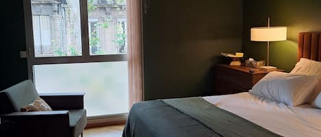 A bedroom with a bed, bedside table, lamp, and a chair.