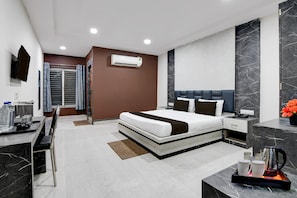 Een moderne hotelkamer met een groot bed, nachtkastjes, een airconditioningapparaat, een bureau met een stoel, en een koffiezetapparaat.