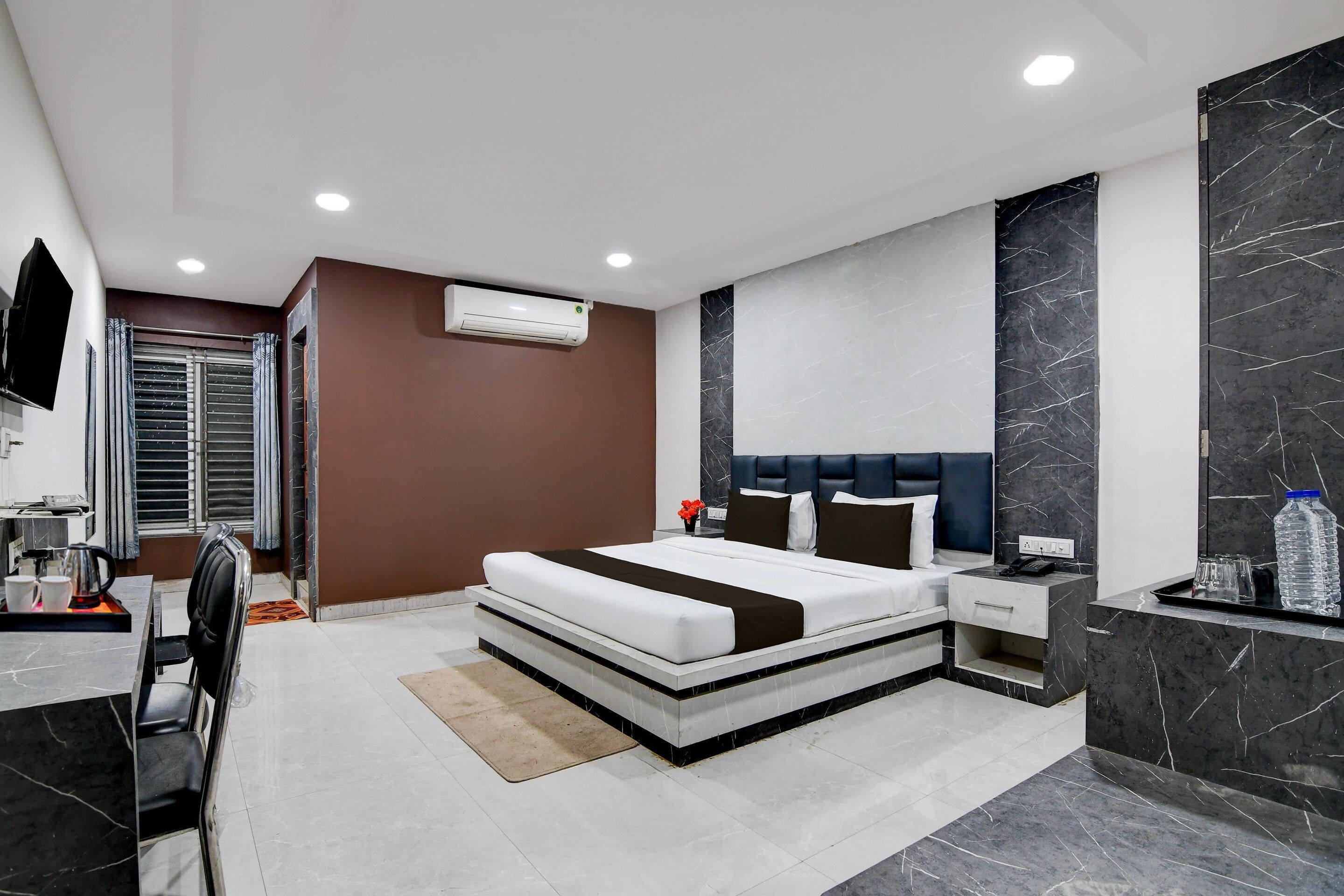 A modern hotel room with a large bed, a bedside table, a built-in TV, and a bathroom with a shower and toilet.