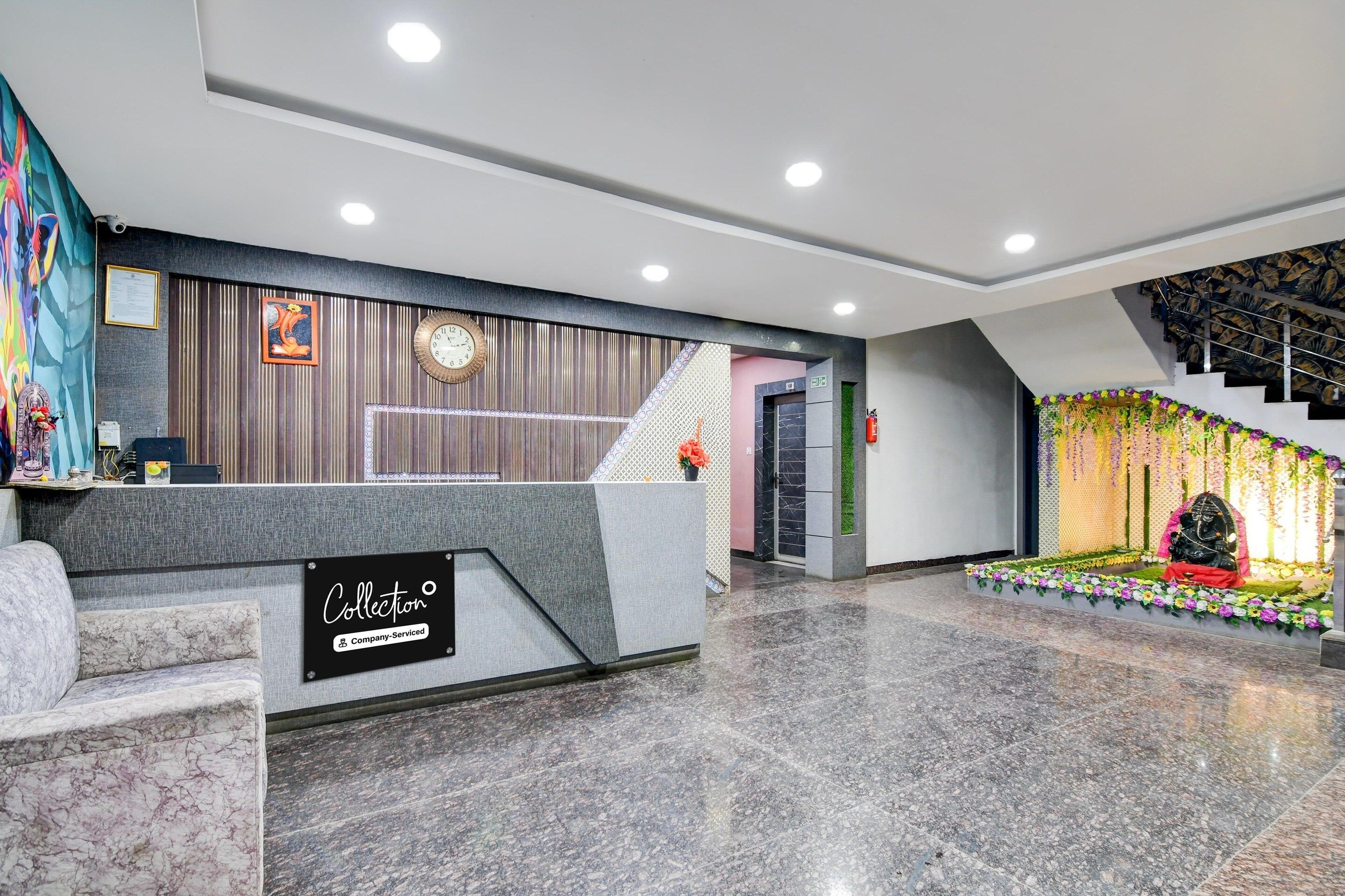 A hotel reception area with a marble floor, a reception desk, a clock, and a staircase with a decorative floral arrangement.