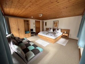 Ein Schlafzimmer mit Holzboden, einem Bett mit gemusterten Betttextilien, einer Couch, einem Kleiderschrank und einem Sessel.