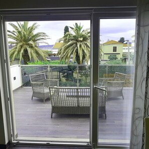 A balcony with wicker furniture and a glass table, overlooking a residential area with palm trees and houses. - New luxurious apartment loreta (Zadar)