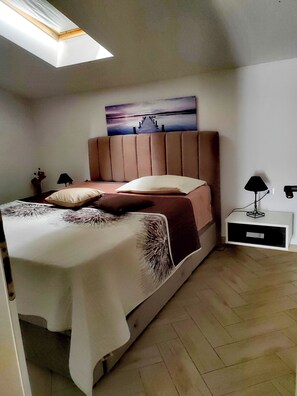 Een slaapkamer met een bed, nachtkastje, lamp en een schilderij aan de muur.