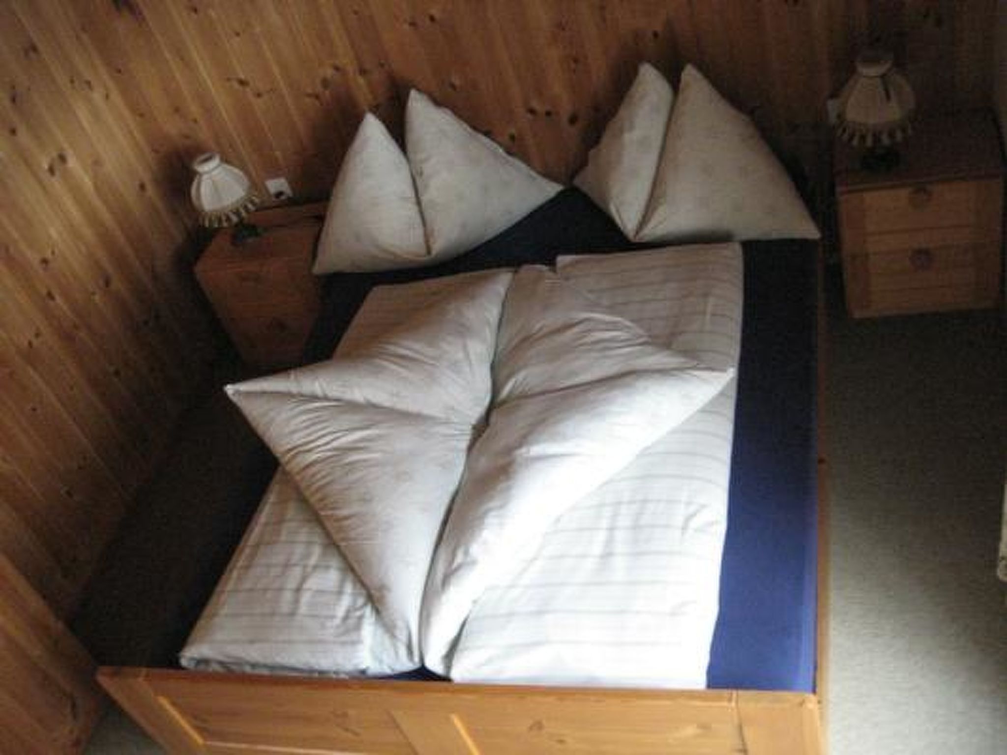 Een houten bed met een blauwe matrasbeschermer en meerdere kussens.