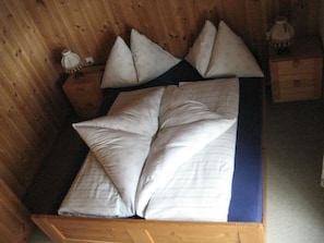 Ein hölzernes Bett mit blauem Bettbezug und mehreren Kissen.