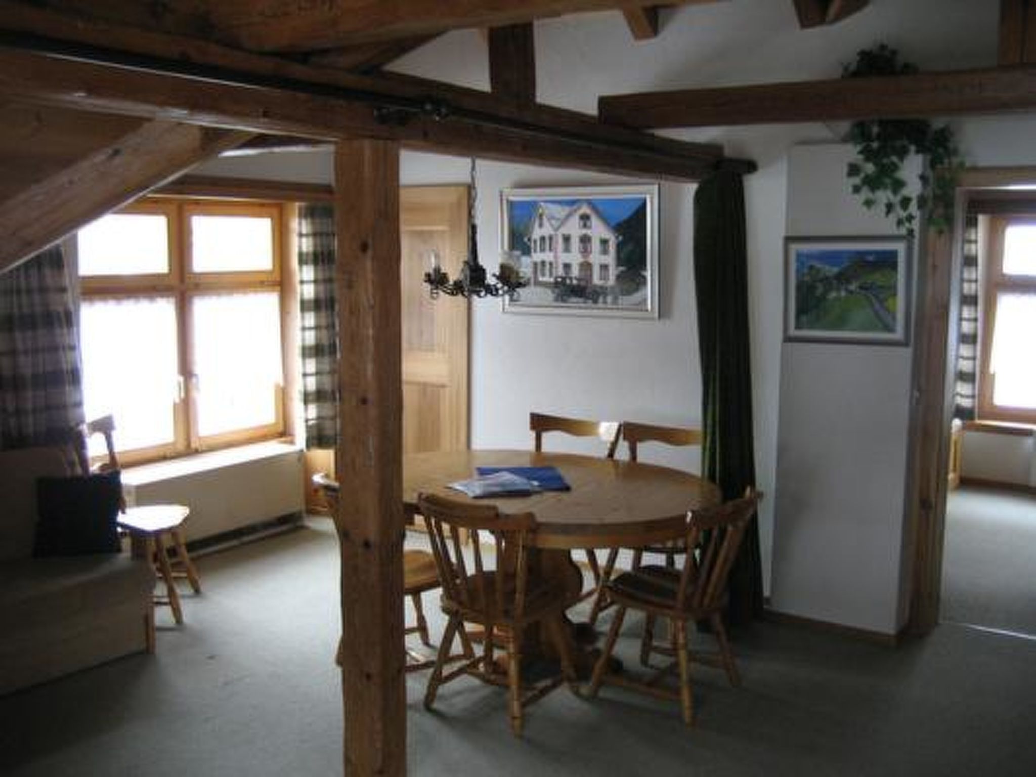 Une pièce avec une table et des chaises en bois, une fenêtre avec des rideaux et un tableau accroché au mur.