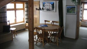 Et værelse med et træbord og stole, et vindue med gardiner og et billede på væggen.