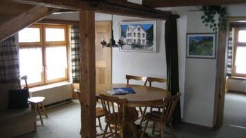 Une pièce avec une table et des chaises en bois, une fenêtre avec des rideaux et un tableau accroché au mur.