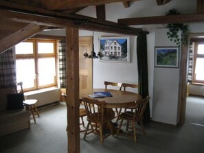 A dining area with a wooden table and chairs, a painting on the wall, and a window with a view.