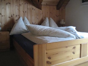 Ein hölzernes Bett mit Kopfstütze, Kissen und einem Nachttisch mit Lampe.