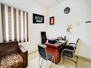 Ein Hotelzimmer mit Schreibtisch, zwei Stühlen, einer Couch, einer Uhr und einem Schild, das anzeigt, dass der Raum von der Firma betreut wird.