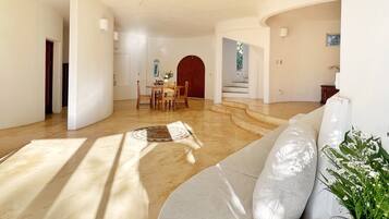 Uma sala de estar ampla, com um sofá grande, uma mesa de jantar com cadeiras e uma escada que dá acesso a um andar superior.