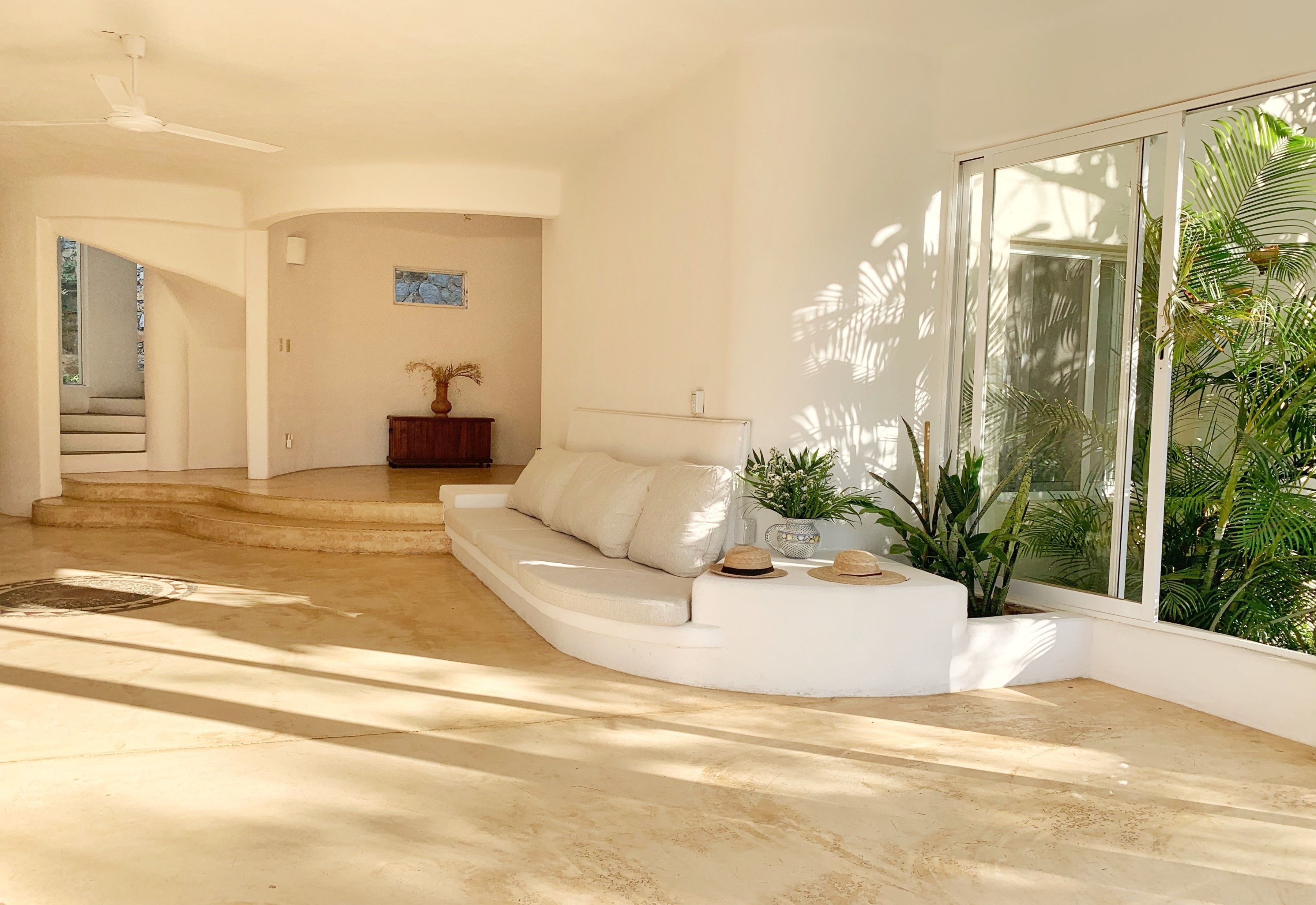 A modern living room with a curved white sofa, a small wooden side table, and a large window with a view of greenery.